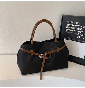 Detail of black nylon tote bag featuring brown leather handles and silver ring buckle
