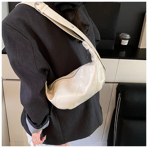 Detail of cream-colored crescent bag with vertical stitching and wide strap on model