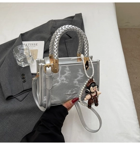 Silver metallic crossbody bag with woven handle and cute doll charm on grey suit jacket