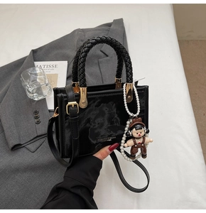 Detail of a black glossy handbag with woven handle, gold hardware and pearl doll charm