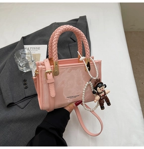 Detailed close-up of a pink glossy square handbag with braided handles and pearl chain