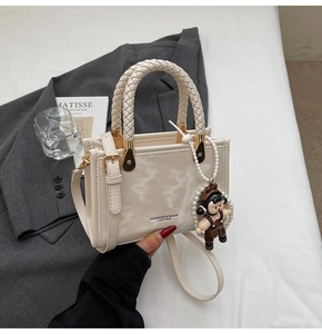 Detail of cream leather square handbag with braided handle and cute pearl doll charm