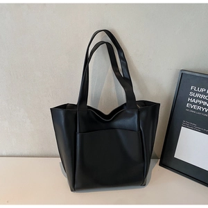Minimalist black tote bag with front pocket detail and slim shoulder straps in studio setting