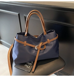 Detail of dark blue nylon tote bag with brown leather straps and silver ring buckle