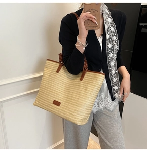 Detailed view of woven straw tote bag with brown leather trim carried by a model