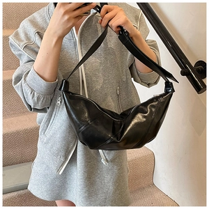 Detail of black glossy leather crossbody dumpling bag with smooth texture and adjustable strap
