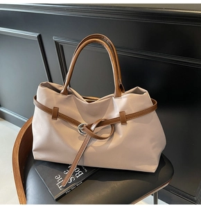 Close-up of beige tote bag with brown straps and silver hardware on a chair