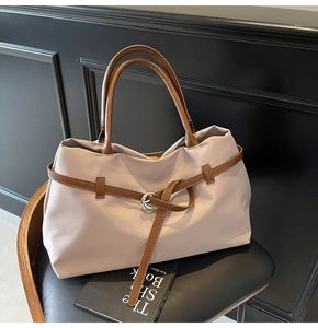 Detail of beige canvas tote bag with dark brown leather handles and silver ring buckle