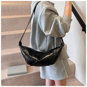 Detail of black glossy crescent bag with pleated design worn on shoulder by a model
