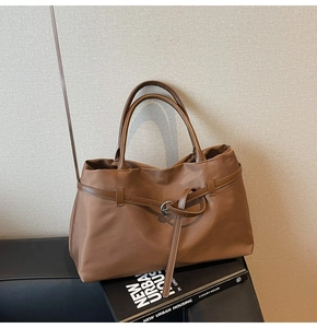 Detail of a brown tote bag with decorative strap and metal ring on a minimalist background