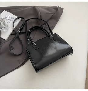 Detail view of a black glossy leather handbag featuring dual handles and adjustable strap