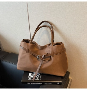 Detail view of large brown tote bag with smooth satin texture and metal ring belt buckle