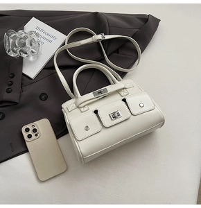 Detail of cream white leather handbag with metal turn-lock closure on grey blazer