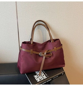 Detail of burgundy tote bag with brown leather straps and silver buckle on a minimal background