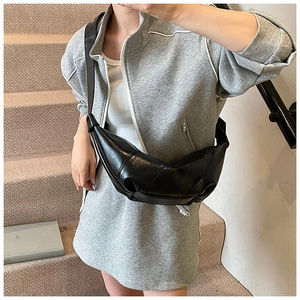Detailed view of black pleated croissant crossbody bag in shiny faux leather on model