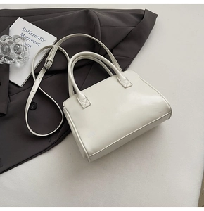 Detail of minimalist cream leather handbag with sturdy top handles and slim shoulder strap