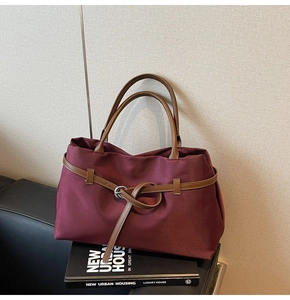 Close-up of burgundy nylon tote bag with brown leather strap on a decorative book