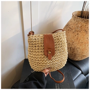 Detail of hand-woven straw crossbody bucket bag with brown leather flap and retro clasp