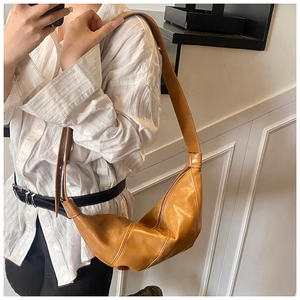 Brown pleated croissant bag worn as a crossbody with a minimalist aesthetic and metal zipper