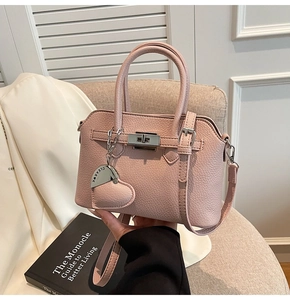 Dettaglio borsa in pelle rosa con chiusura argento e ciondolo a cuore su divano
