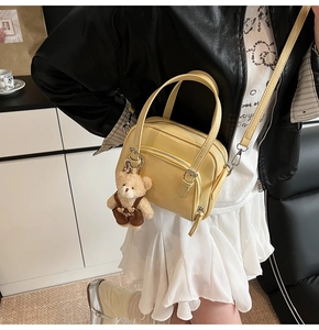 Detail showing the glossy yellow shell bag with its plush bear charm and metallic hardware