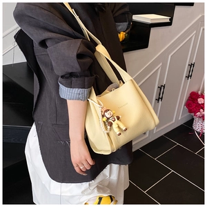 Close-up of yellow litchi pattern handbag featuring Fashion print and a cute doll charm