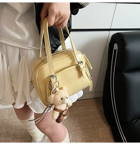 Detail view of a yellow oil-wax leather Boston bag with teddy bear charm and metal zipper