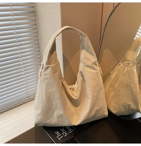 Detail of a large cream nylon hobo bag showing multiple zippers and a pleated texture