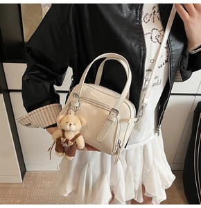 Detail of white glossy shell bag with cute plush bear charm and crossbody strap