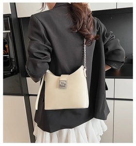 Détail d'un sac bandoulière blanc crème en cuir avec chaîne argentée sur blazer noir