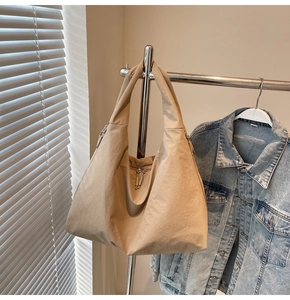 Detail view of khaki canvas tote bag with front zipper pocket hanging on a metal rack