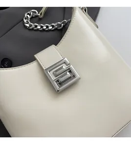 Gros plan d'un sac bandoulière en cuir beige avec chaîne argentée et fermoir carré en métal
