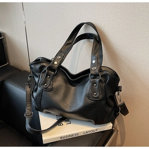 Close-up of black leather tote bag featuring lychee texture and silver rivet hardware