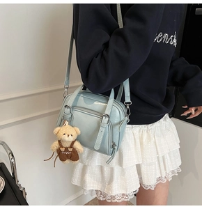 Detail of light blue shell bag with glossy finish and cute teddy bear charm