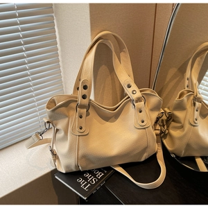 Close-up of beige lychee grain leather tote bag with rivet handle details and strap