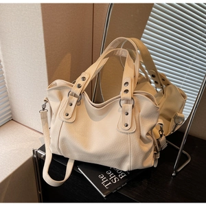 Detail of cream tote bag featuring pebbled leather texture and metal rivet accents