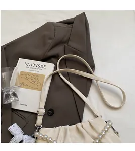 Detail of cream pleated cloud bag featuring pearl chain strap and long shoulder strap