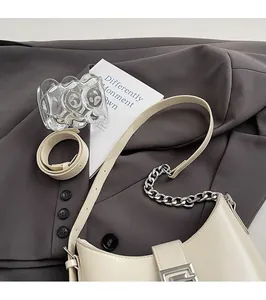 Détail du sac seau crème avec chaîne argentée et boucle magnétique sur une veste de costume