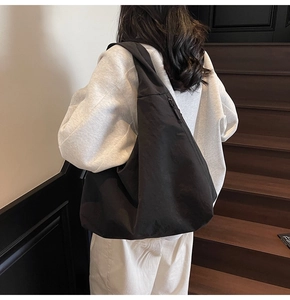 Detail shot of a black canvas crescent tote bag worn by a model in casual white outfit