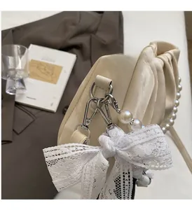 Close-up of cream pleated handbag with pearl handle and lace bow charm on a blazer