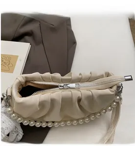Detail of creamy white pleated bag with smooth silver zipper and pearl handle accent