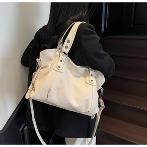 Close-up of a cream oversized tote bag with silver metal rings and textured faux leather