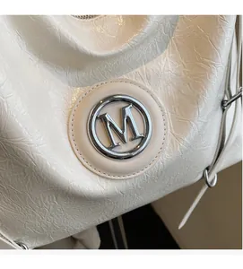 Détail du cuir brillant plissé et du logo M argenté sur un sac fourre-tout beige