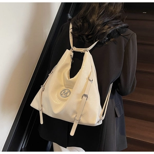 Détail du sac à dos en cuir verni beige avec logo M argenté porté par un mannequin