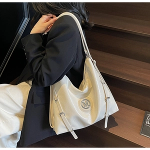 Gros plan sur le sac fourre-tout blanc avec logo M argenté et sangles en cuir sur bois