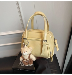 Dettaglio di borsa in pelle lucida giallo chiaro con ciondolo a orsetto e fibbie in metallo