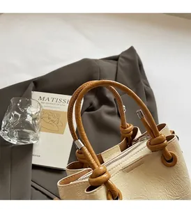 Detail of knotted brown leather handle and cream textured PU fabric on bucket bag
