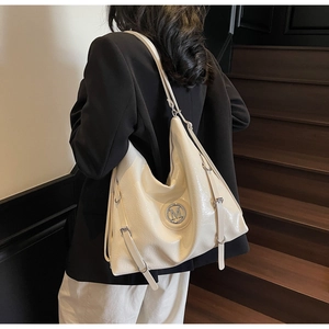 Détail d'un sac cabas en similicuir blanc crème avec logo M en métal sur un escalier en bois