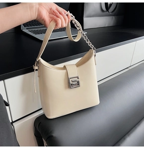 Close-up of beige shoulder bag featuring silver metal G-buckle and chain strap detail
