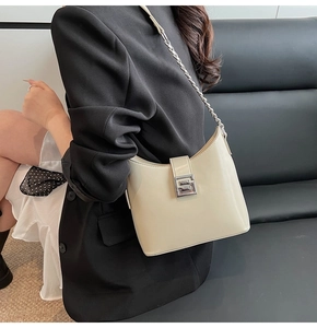 Detailed view of cream patent leather bag with silver chain strap and metal buckle